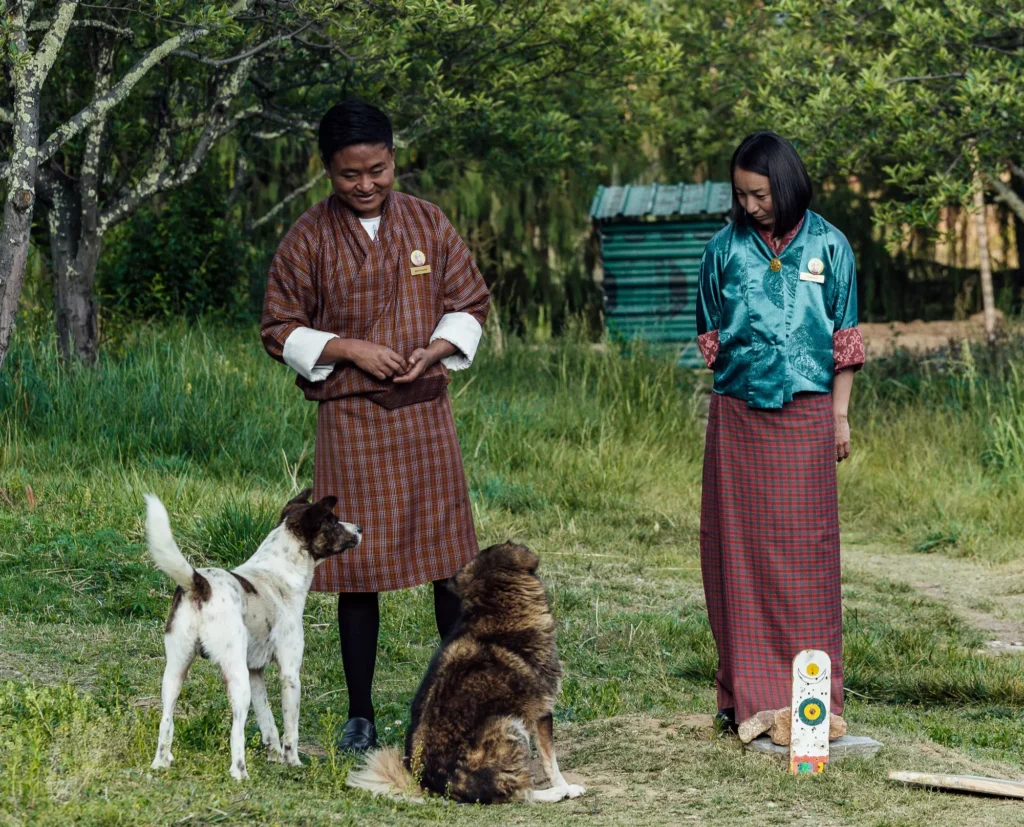 a couple of people standing in a grassy area with a dog