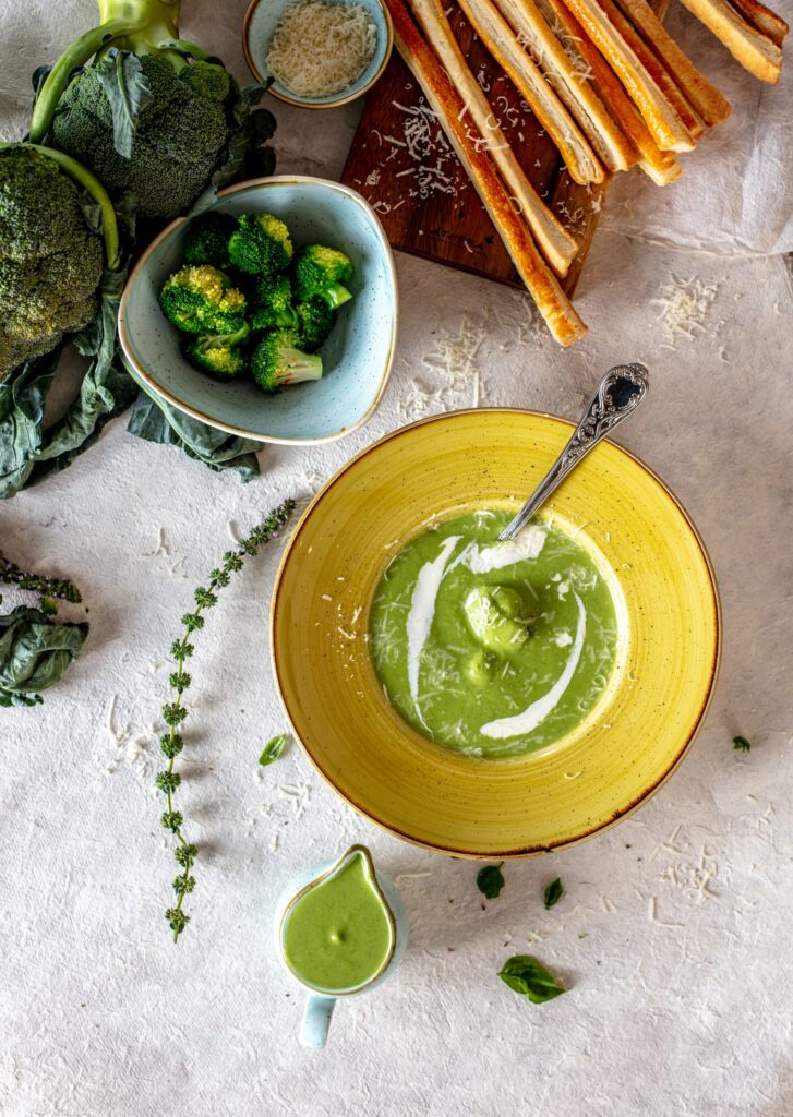 a bowl of green soup with a spoon and a bowl of broccoli