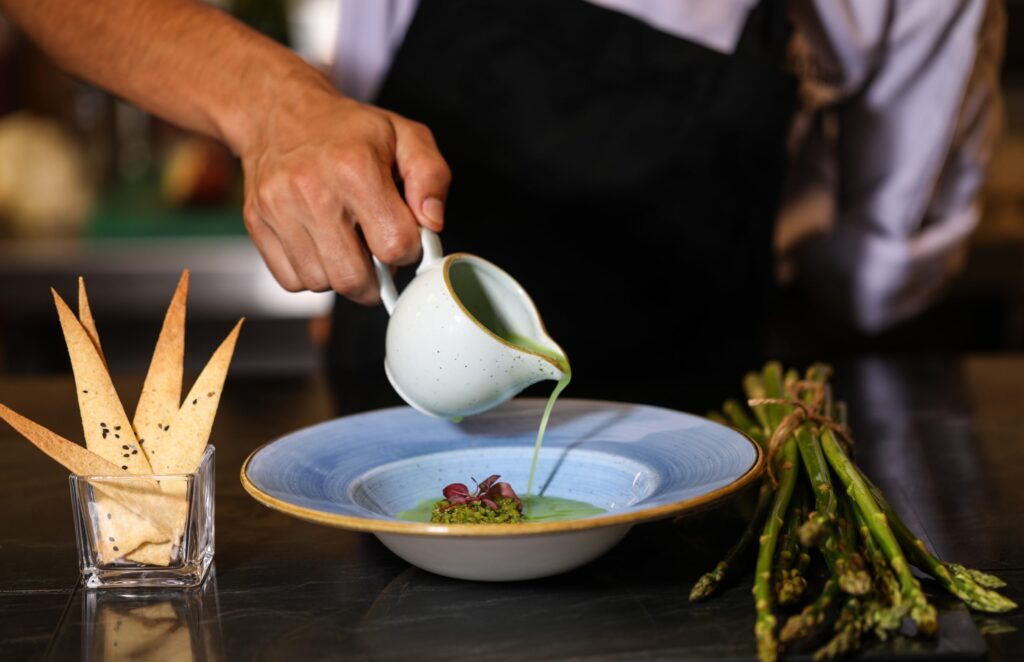 a person pouring green liquid into a bowl of food