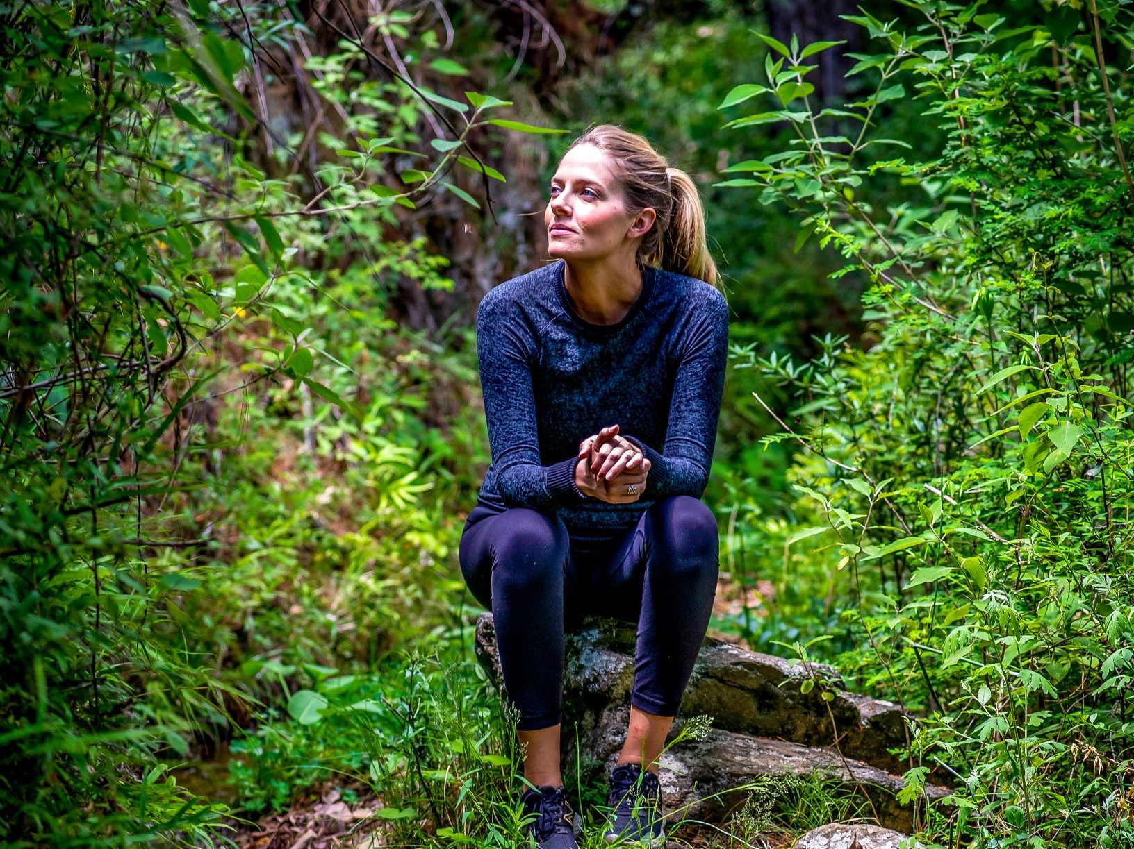 blond woman sitting in a forest in sports clothing